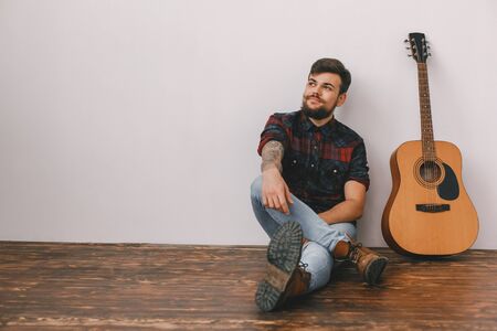 Young guitarist hipster at home with guitar sitting thoughtfulの写真素材