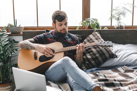 Young guitarist hipster at home with guitar in bedroom playing seriousの写真素材