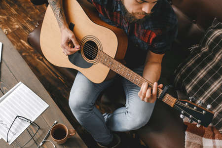 Young guitarist hipster at home playing guitar top view close-upの写真素材