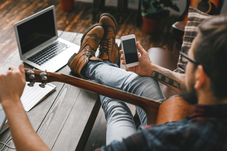Young guitarist hipster at home with guitar tuning using app close-upの写真素材