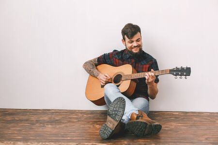Young guitarist hipster at home sitting on the floor playing guitar smilingの写真素材