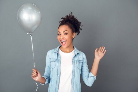 Young african woman isolated on grey wall studio casual daily lifestyle birthday balloonの写真素材