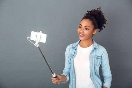 Young african woman isolated on grey wall studio casual daily lifestyle holding monopodの写真素材