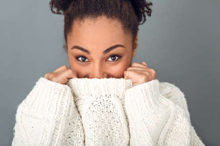 Young african woman isolated on grey wall studio winter concept cover face with collarの写真素材