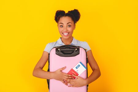 Young african woman isolated on yellow wall studio cute style traveler concept holding baggageの写真素材