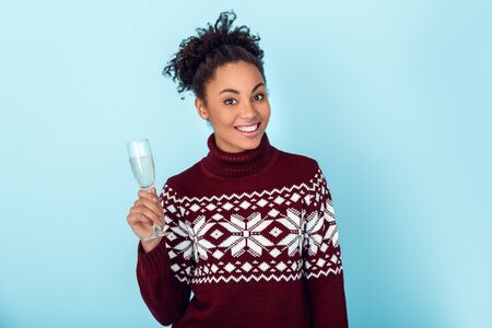 Young african woman isolated on blue wall studio winter concept glass of champagneの写真素材