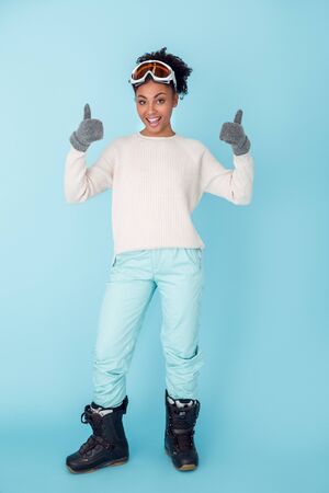 Young african woman isolated on blue wall studio winter sport concept thumbs upの写真素材