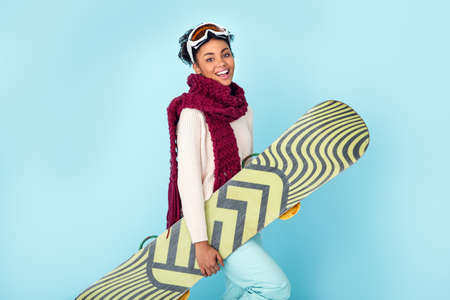 Young african woman isolated on blue wall studio winter sport snowboarding concept walkingの写真素材