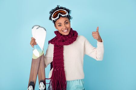 Young african woman isolated on blue wall studio winter sport skiing thumb upの写真素材