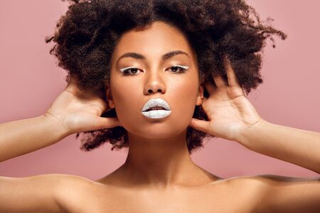Young african woman isolated on pink wall studio fashion stylish makeup holding hair upの写真素材