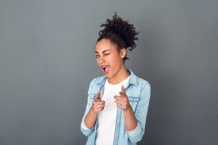 Young african woman isolated on grey wall studio casual daily lifestyle pointing at cameraの写真素材