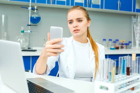 Young chemistry teacher in school laboratory workplace holding smartphoneの写真素材