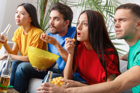 Group of friends sport fans watching match in colorful shirts excited concentrated close-upの写真素材