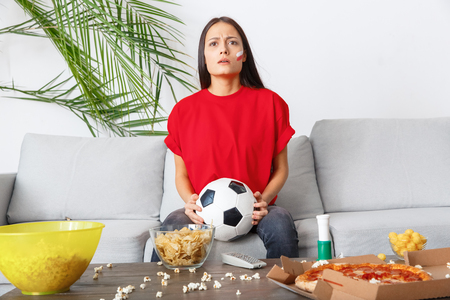 Young woman sport fan watching match in a red t-shirt confusedの写真素材