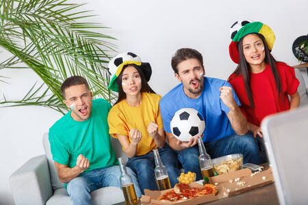 Group of friends sport fans watching match in colorful shirts supporting teamの写真素材