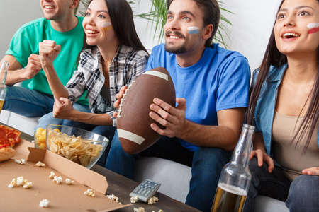 Group of friends sport fans watching match in colorful shirts american footballの写真素材
