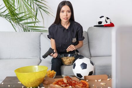 Young woman police officer sport fan watching match eating snacksの写真素材