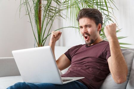 Young man sport fan watching match on laptop goalの写真素材
