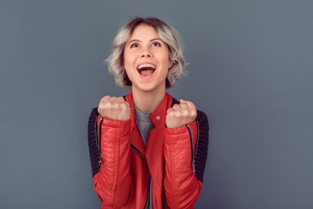 Young woman standing in leather jacket isolated on grey wall happyの写真素材