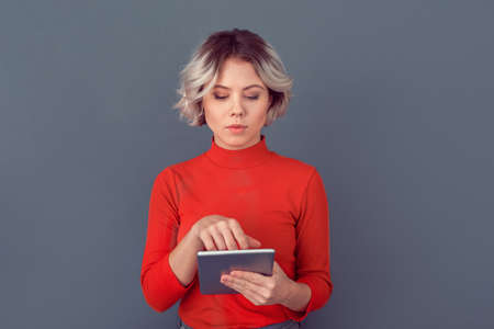 Young woman in a red blouse isolated on grey wall working on digital tabletの写真素材
