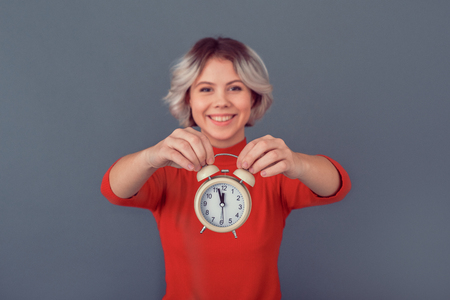 Young woman in a red blouse isolated on grey wall time to workの写真素材
