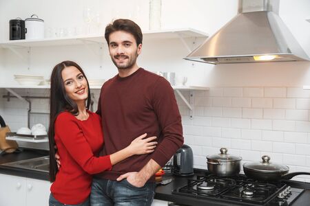 Young couple having romantic evening at home in the kitchen hugging looking cameraの写真素材