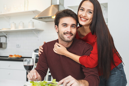Young couple having romantic evening at home in the kitchen hugging looking cameraの写真素材