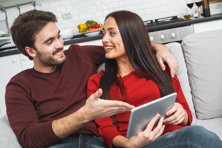 Young couple having romantic evening at home showing app on digital tabletの写真素材