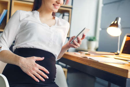 Pregnant business woman working at office motherhood sitting browsing smartphoneの写真素材