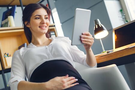 Pregnant business woman working at office motherhood sitting watching videos on digital tabletの写真素材