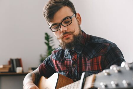 Young guitarist hipster at home with guitar playing thoughtful close-up