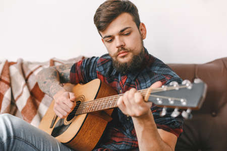 Young guitarist hipster at home sitting playing guitar seriousの写真素材