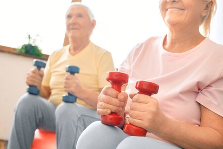 Senior couple exercise together at home doing aerobics with dubbells close-up