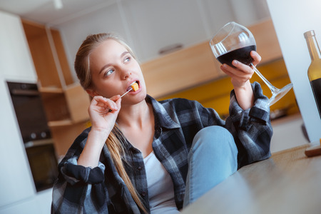 Young woman at home in the kitchen drinking wine dreamingの写真素材