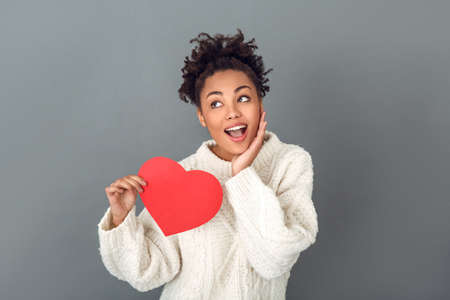 Young african woman isolated on grey wall studio winter concept holding heart dreamingの写真素材