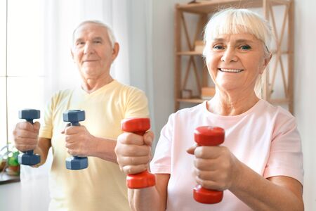 Senior couple exercise together at home health care with dumbbells looking cameraの写真素材