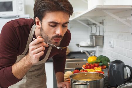 Young man cooking romantic dinner at home taste soupの写真素材