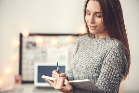 Young woman freelancer indoors home office concept winter atmosphere blurred background writing in plannerの写真素材