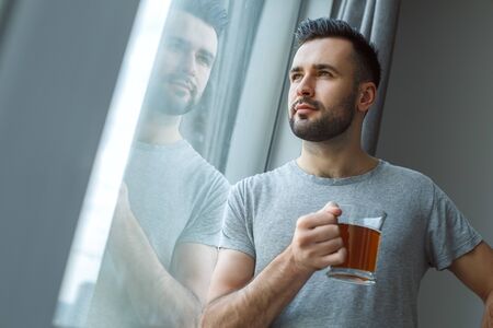 Bachelor man daily routine standing near the window single lifestyle concept drinking tea close-upの写真素材