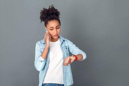 Young african woman isolated on grey wall studio casual daily lifestyle checking timeの写真素材