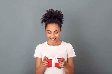 Young african woman isolated on grey wall studio celebration concept looking at presentの写真素材
