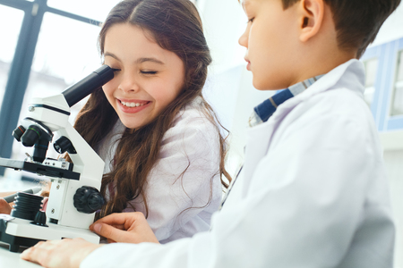 Little kids learning chemistry in school laboratory working with microscopeの写真素材