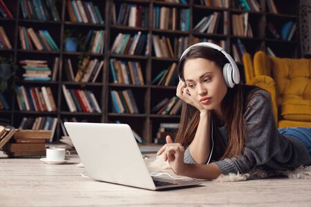 Young woman writer in library at home creative occupation lying listening musicの写真素材
