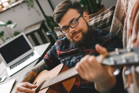 Young guitarist hipster at home with guitar lying playing close-upの写真素材