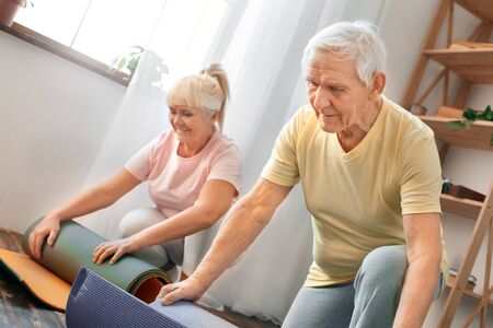 Senior couple exercise together at home health care rolling yoga mat thinkingの写真素材