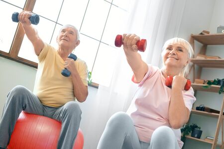 Senior couple exercise together at home doing aerobics with dubbells in frontの写真素材