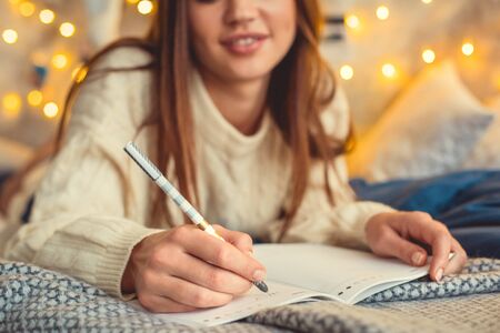 Young woman weekend at home decorated bedroom writing in planner close-upの写真素材