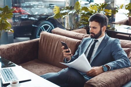 Businessman sitting in a business center restaurant browsing smartphone concentratedの写真素材