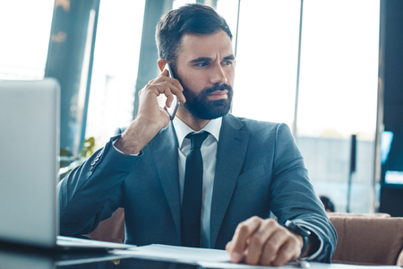 Businessman sitting in a business center restaurant smartphone communication listeningの写真素材