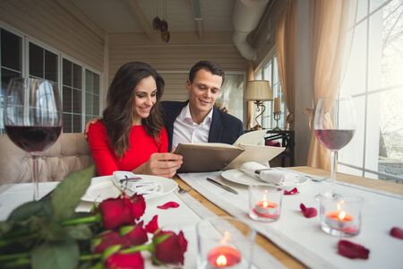 Young couple having romantic dinner in the restaurant holding menu choosingの写真素材